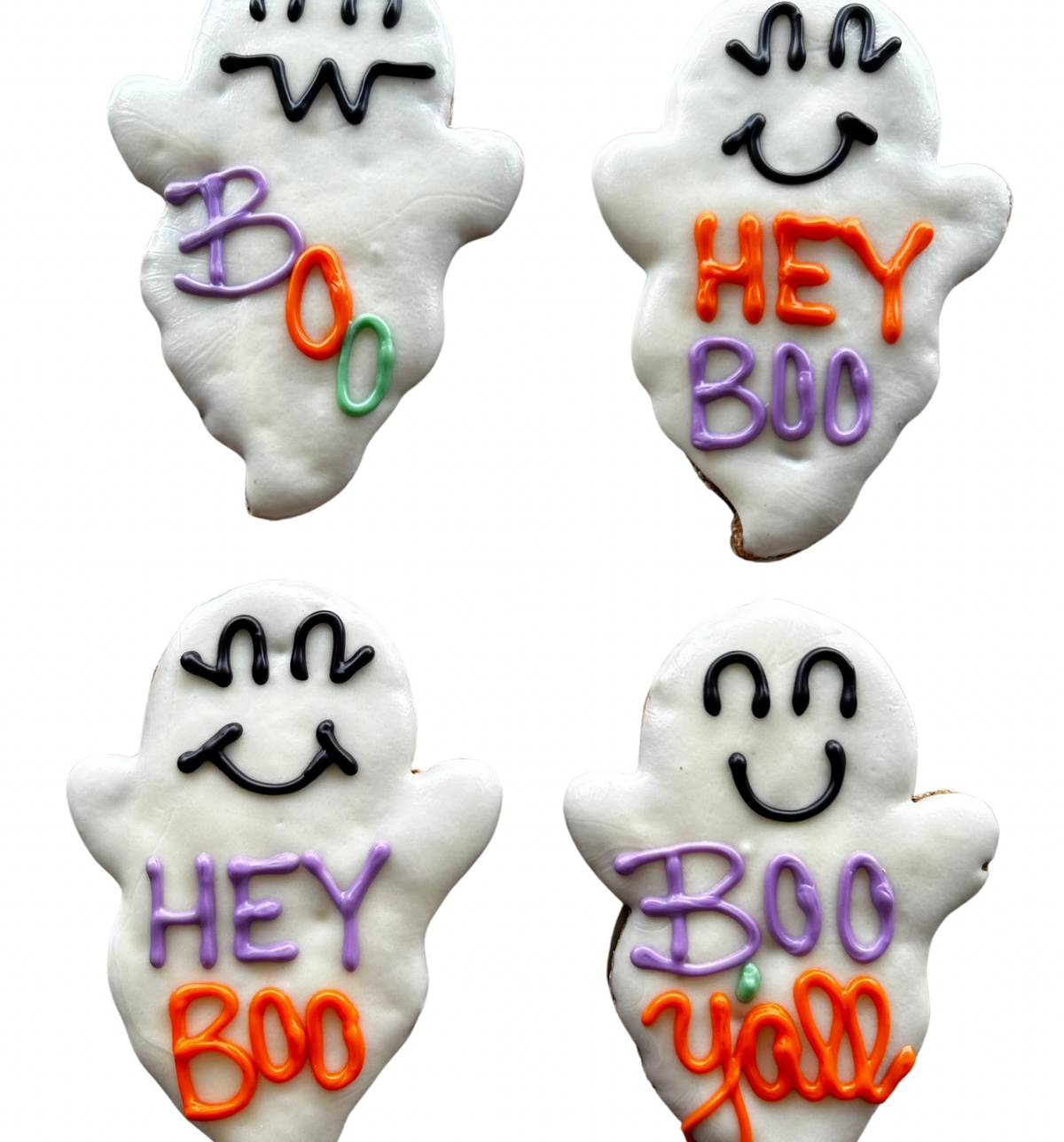 Two white ghost-shaped dog cookies with smiling faces and purple and orange lettering reading Hey Boo and Boo Y’all on a wooden plate.