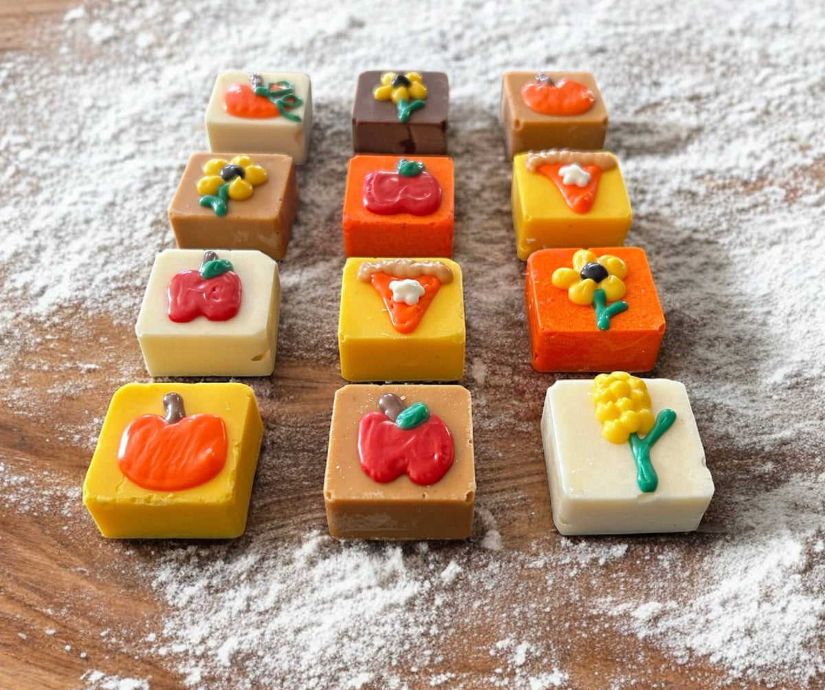 Square dog truffles in white, tan, brown, orange, and yellow topped with pumpkins, apples, flowers, and pie-slice decorations.