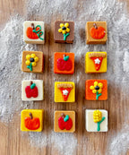 Square dog truffles in white, tan, brown, orange, and yellow topped with pumpkins, apples, flowers, and pie-slice decorations.
