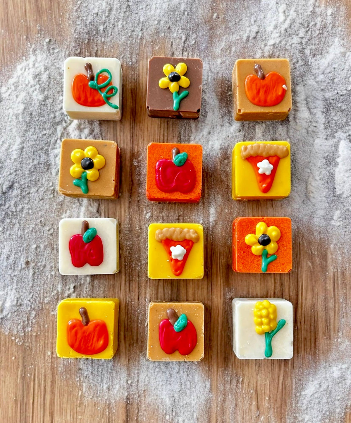 Square dog truffles in white, tan, brown, orange, and yellow topped with pumpkins, apples, flowers, and pie-slice decorations.