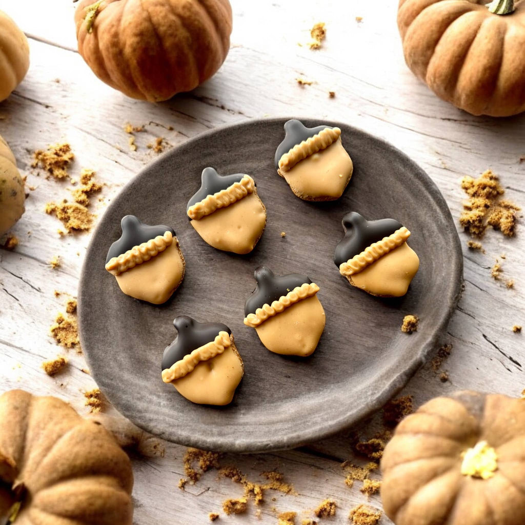 Six acorn-shaped dog cookies with tan decoration, dark caps, and piped trim arranged on a round gray plate.