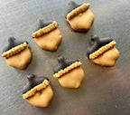 Six acorn-shaped dog cookies with tan decoration, dark caps, and piped trim arranged on a round gray plate.