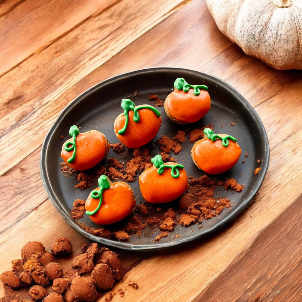 Six pumpkin-shaped dog cookies decorated in orange with green stems and curling vines on a round wooden tray.