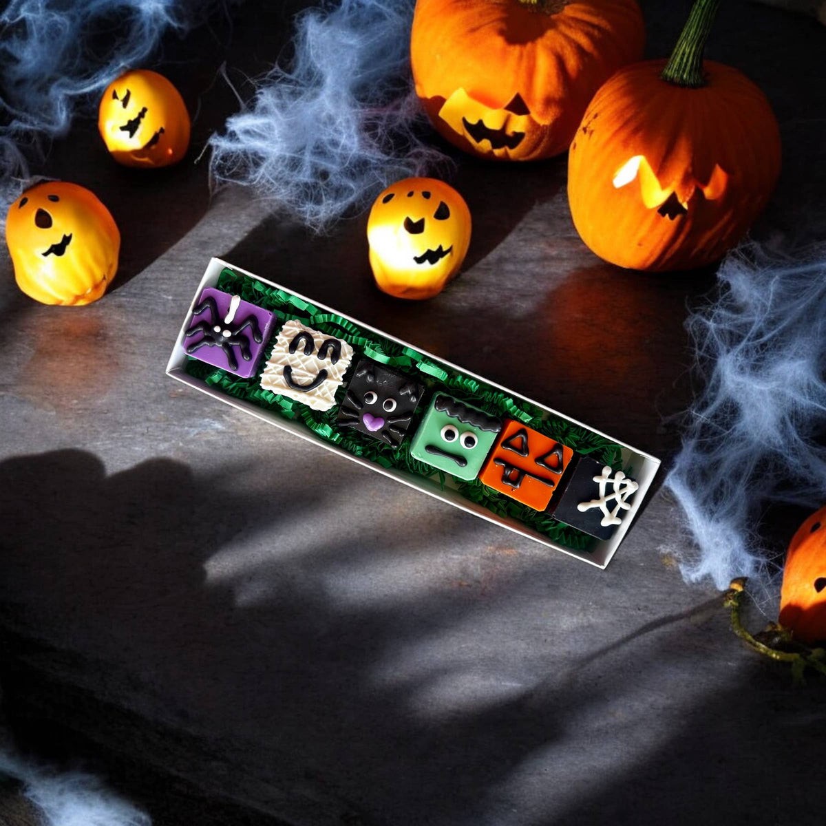 Assorted Halloween dog truffles with ghost, monster, pumpkin, and spiderweb designs displayed on a rectangular tray.